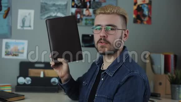 英俊时尚的男人快乐的脸拿着书竖起大拇指有黄头发的嬉皮士为一本书做广告家庭视频的预览图