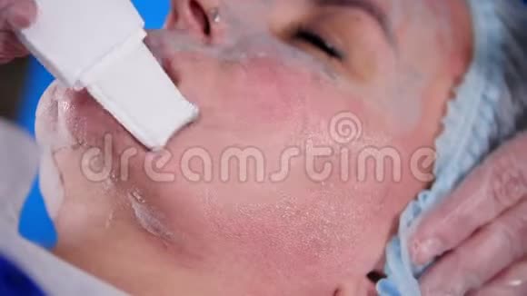 美容诊所年轻女性由按摩师用面霜和工具在面膜中进行专业的面部按摩视频的预览图