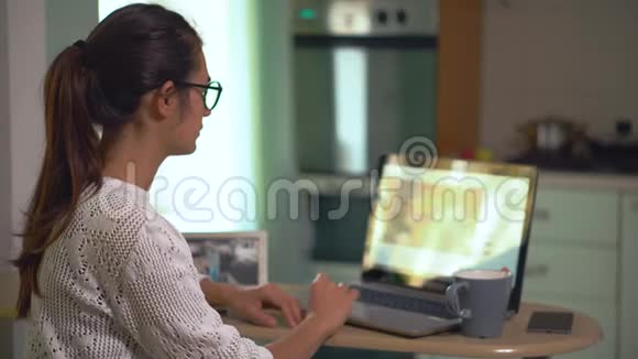 女孩坐在厨房自由职业者在家工作在笔记本电脑上搜索信息喝咖啡视频的预览图