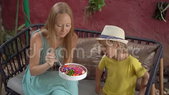 年轻的女人和她的小儿子坐在一家漂亮的咖啡馆里享受着碗里五颜六色的麦片粥健康饮食视频的预览图