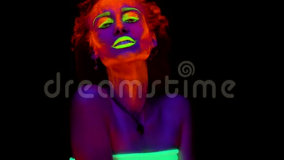 一个美丽的年轻女孩画着发光的油漆摆在黑色的灯光下说话一个漂亮的女人视频的预览图
