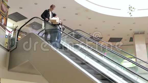 年轻的家庭在购物中心乘坐自动扶梯手里拿着袋子视频的预览图