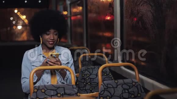 漂亮的非洲裔美国年轻女性使用智能手机乘坐公共交通工具看着窗外夜晚视频的预览图