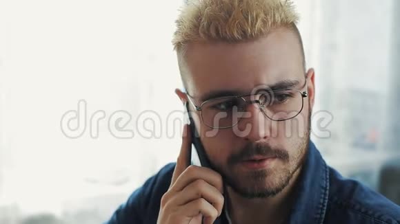 年轻迷人的商人戴着黄色头发的眼镜在电话里交谈坐在办公桌前视频的预览图