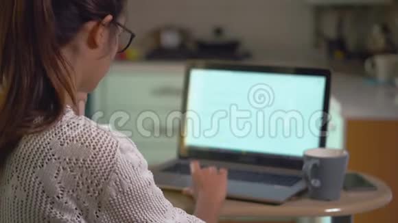女孩坐在厨房里在网上学习在笔记本电脑上搜索信息喝咖啡视频的预览图