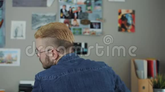 白种人的肖像戴着眼镜发型时尚黄色头发坐在家里的办公桌上回头看视频的预览图