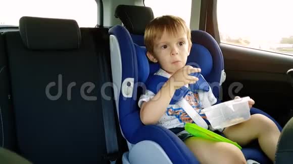 小蹒跚学步的男孩在车里吃饭的4k视频儿童坐在安全的汽车座椅上吃饼干视频的预览图