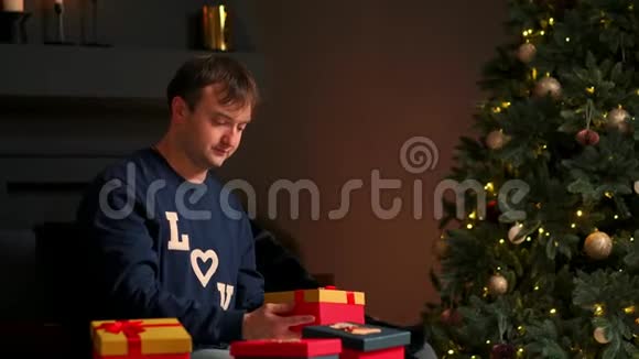 手里拿着圣诞礼物的年轻人坐在沙发上打开礼物视频的预览图