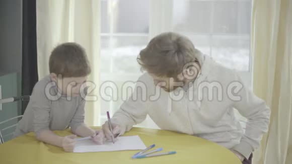 大胡子的父亲和他的小儿子坐在客厅的桌子上画着纸父子关系视频的预览图