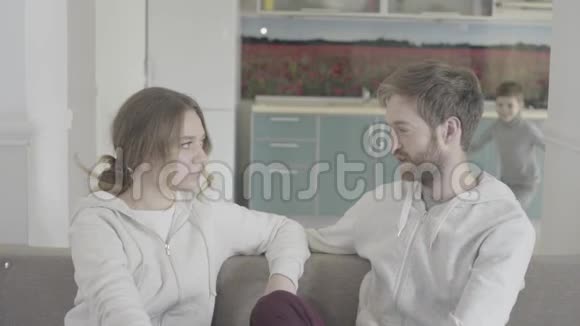 漂亮的夫妇坐在沙发上交谈小儿子来拥抱父母快乐的家人挥手视频的预览图