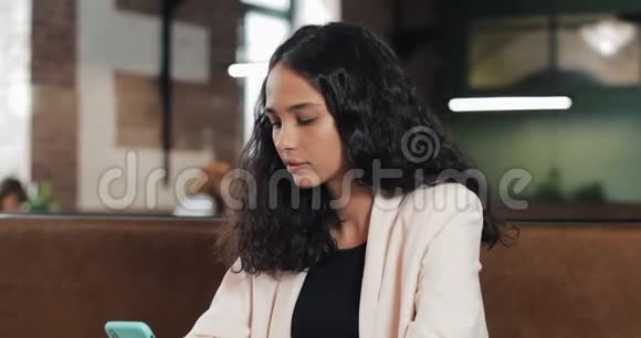 成功商业女性的肖像她手里拿着智能手机看着相机在工作时微笑着视频的预览图