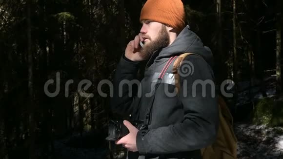 一个戴着帽子的长胡子的人在针叶林里用手机说话细胞通讯的概念视频的预览图