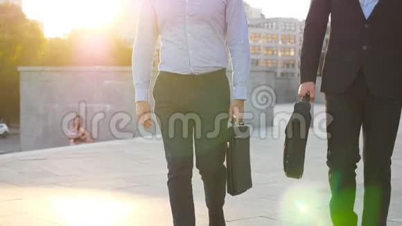 两个商人带着公文包走在城市街道上背景是太阳耀斑合作伙伴一起上下班视频的预览图