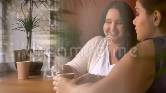 两个白种人的大女孩在咖啡馆的窗口边笑着兴奋地看着智能手机视频的预览图