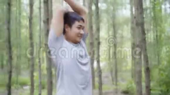 健康英俊的年轻亚洲运动员穿着运动服装腿暖和伸展手臂准备在森林里跑步视频的预览图