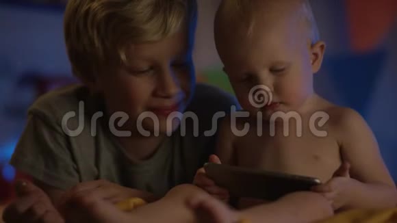 可爱的孩子只是坐在不好的地方用电话看动画片微笑着他的哥哥做伴视频的预览图