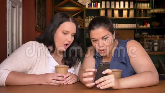 两个大白种人女人惊讶地看着手机室内有两杯饮料视频的预览图