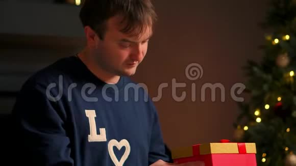 手里拿着圣诞礼物的年轻人坐在沙发上打开礼物视频的预览图