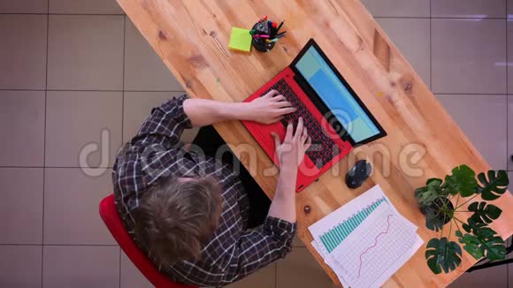 一位年轻的高加索商人在桌上的笔记本电脑上打字并在办公室里分析图表的特写镜头视频的预览图