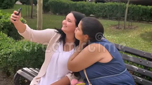 两个肥胖的白种人女朋友坐在公园的长椅上一边自拍一边笑着视频的预览图
