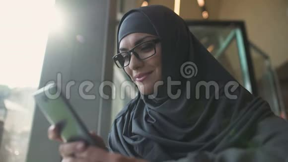 在咖啡馆里微笑的阿拉伯女士在电话聊天申请网上购物视频的预览图