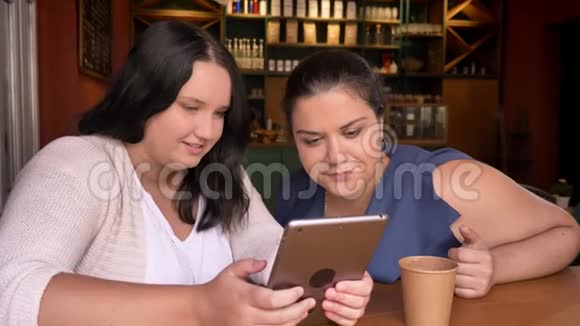 两个吃得好的白种人女朋友看了一眼planshet然后坐在咖啡馆里轻轻地拍了一下视频的预览图