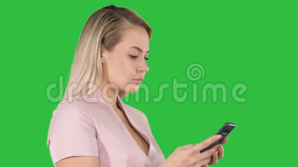 在绿色屏幕上Chroma键在智能手机上发送信息的欢快年轻女人的肖像视频的预览图