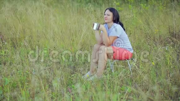 年轻女子坐在森林的空地上喝茶视频的预览图