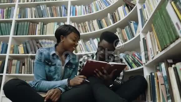 多莉拍摄的非洲年轻男女学生坐在书架旁的地板上看书视频的预览图