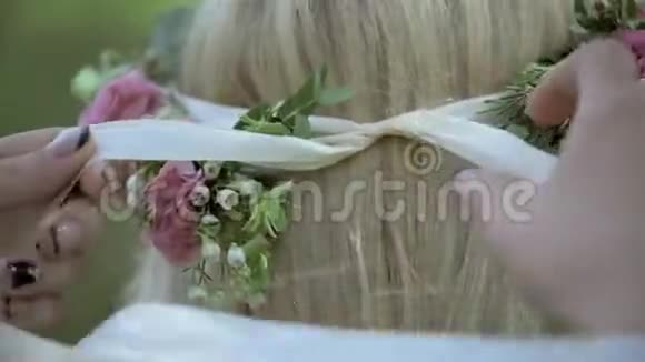 新娘的伴娘在婚礼当天为漂亮的金发新娘系着头巾头上的花圈视频的预览图