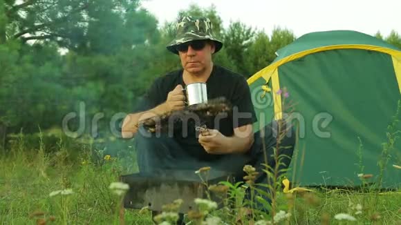一个人靠近帐篷喝着茶在烤架上翻着肉视频的预览图
