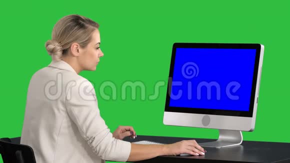 年轻女性在办公室工作坐在办公桌前看着绿色屏幕上的监视器Chroma键蓝色屏幕模拟视频的预览图