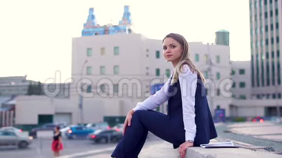 美丽的女孩穿着商务套装在市中心坐在楼梯上看着镜头视频的预览图
