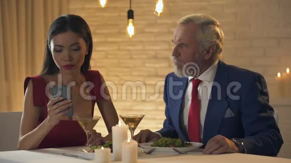 女孩和无聊的老人坐在餐馆里打电话聊天糟糕的约会视频的预览图