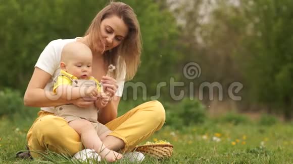 年轻的妈妈带着小宝宝在公园里孩子手里拿着蒲公英黄绿色配色方案母亲节视频的预览图