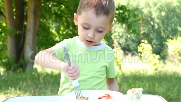 孩子吃烧烤坐在绿林背景的桌子旁视频的预览图
