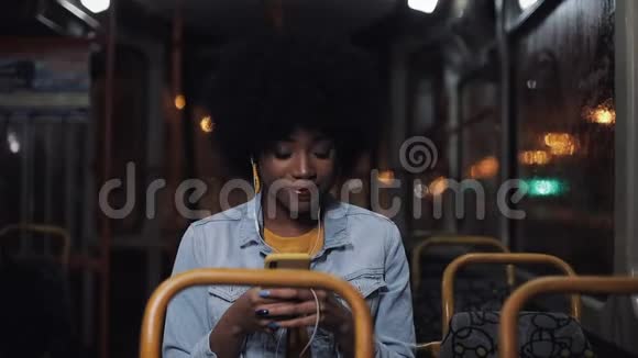 漂亮的非洲裔美国年轻女性使用智能手机乘坐公共交通工具看着窗外夜晚视频的预览图