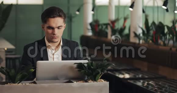 年轻严肃的商人坐在舒适的咖啡馆里用笔记本电脑工作从事项目工作的自由职业者或学生视频的预览图