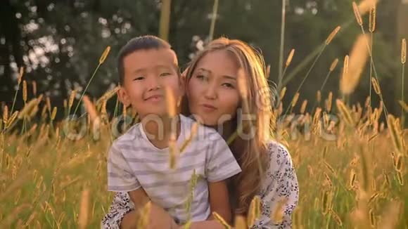 微笑的亚洲母亲和她的小儿子坐在草地上拥抱在什么田野景观上视频的预览图