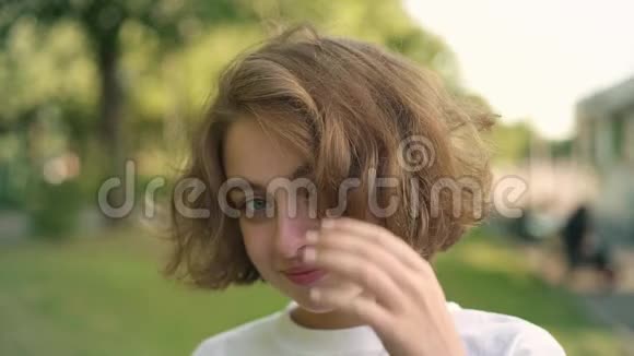 可爱的年轻女子微笑着眨眼看着夏天公园里的摄像机视频的预览图