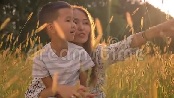 可爱的亚洲家庭可爱的男孩和他的母亲在田野里坐在黄色的草地上愉快地交谈视频的预览图