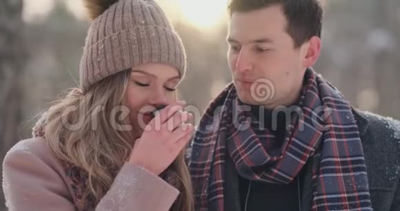 穿着外套和围巾的漂亮时髦的夫妇在冬天的森林里喝热水瓶里的茶视频的预览图
