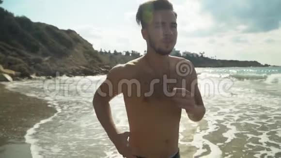 早晨一个留着胡子的年轻人沿着海滨奔跑在海边慢跑慢动作健康生活方式视频的预览图