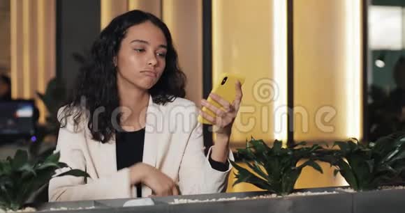 疲惫的商务女性在咖啡馆里使用智能手机坐在现代同事间喝咖啡的女孩视频的预览图