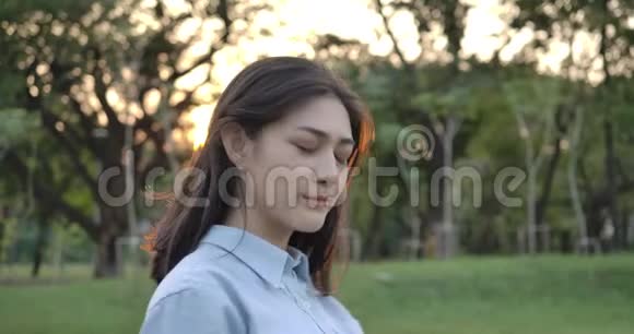 年轻迷人的亚洲女人的肖像在夕阳下的夏日公园里开心地微笑着进入镜头视频的预览图