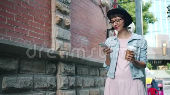 微笑的女孩用智能手机慢动作拿着饮料在户外散步视频的预览图