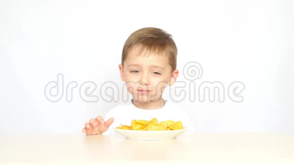 一个快乐和快乐的孩子在白色背景下坐在桌子旁吃薯片视频的预览图