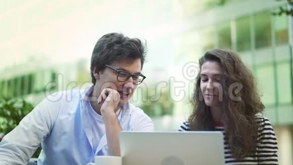 成功的年轻人在夏季咖啡馆里坐着笔记本电脑笑着视频的预览图