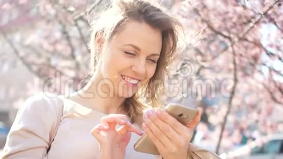 漂亮的年轻女人手里拿着智能手机外面的肖像在盛开的春天的背景下视频的预览图