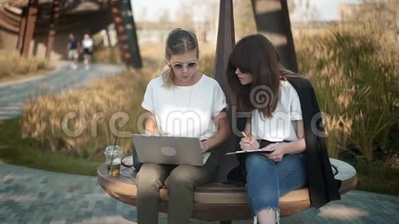 两个有魅力又聪明的女人用笔记本电脑工作或者在夏季公园学习视频的预览图